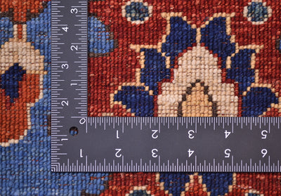 Close-up of the hand-knotted underside of an Afghan Aryana blue rug with a dark metal L-shaped ruler placed over it to show scale, featuring a red, blue, and beige floral design.