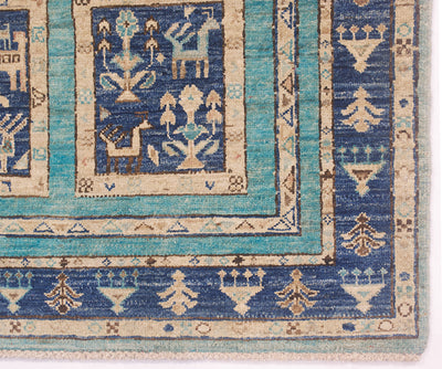 Close-up of a handwoven Afghan rug corner showing geometric and stylised motifs in blue, turquoise, beige, and brown on a white background.