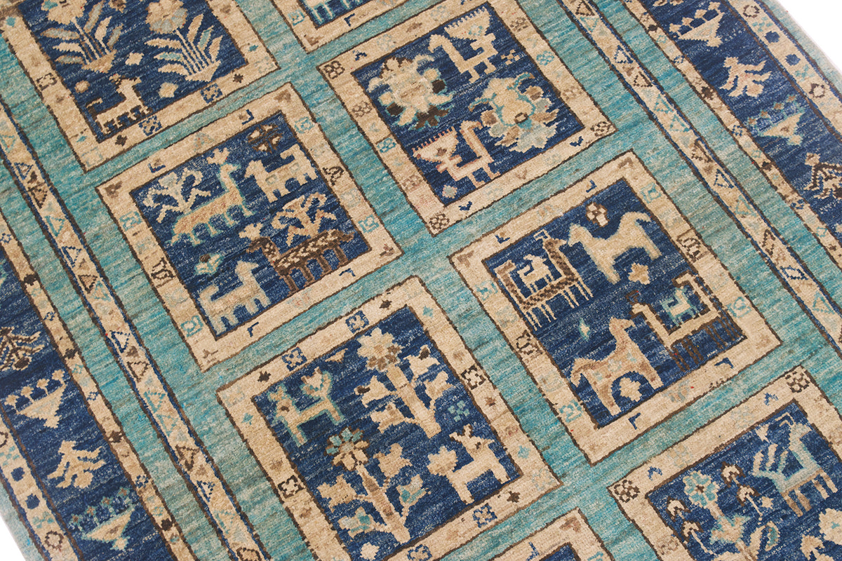 A close-up of a patterned handmade Afghan rug featuring blue and turquoise fields with beige and cream geometric and animal motifs arranged in square panels.