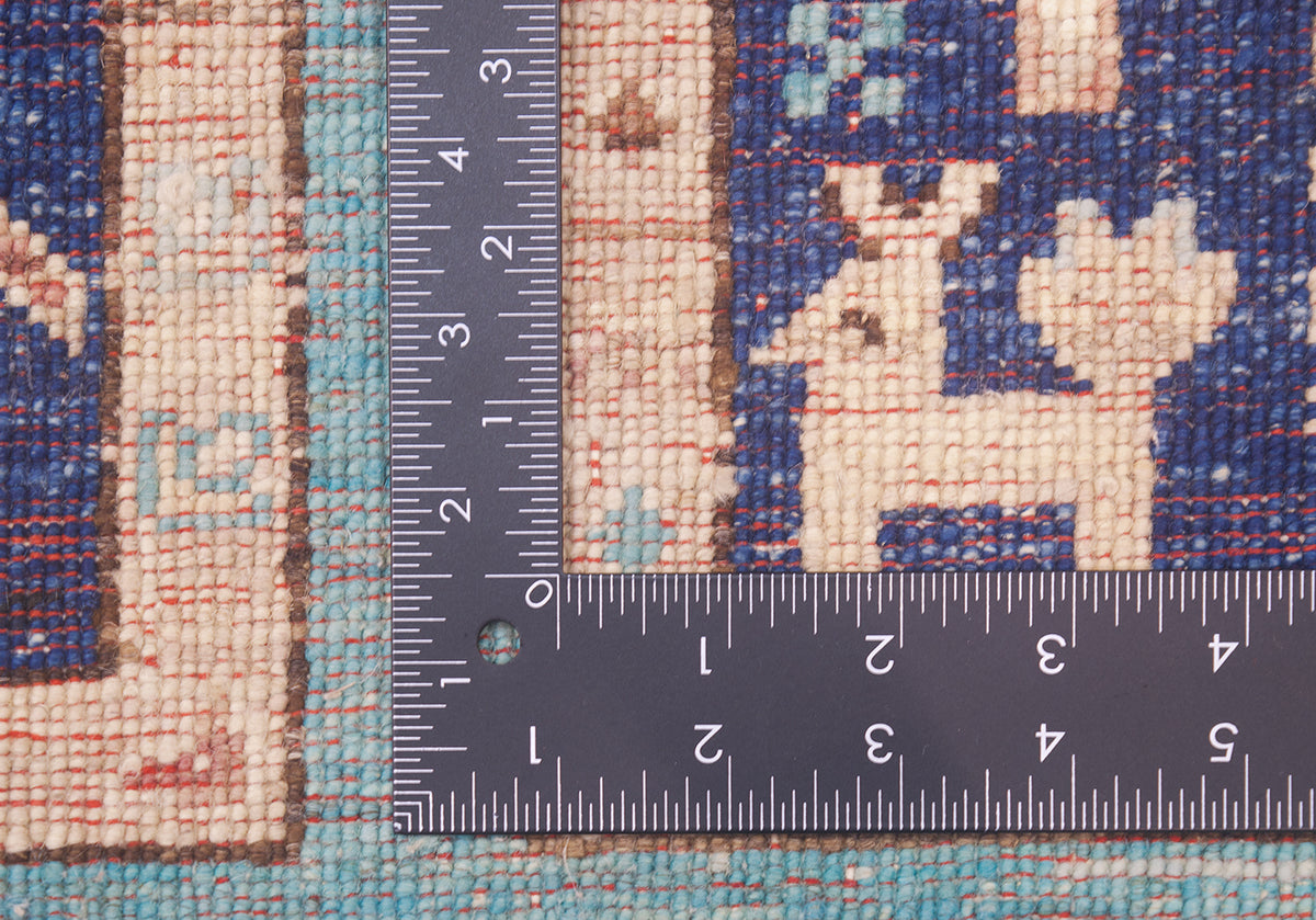 Close-up of the hand-knotted weave of a patterned Afghan Aryana rug with a dark metal ruler placed vertically and horizontally to show the scale of the weave and design.