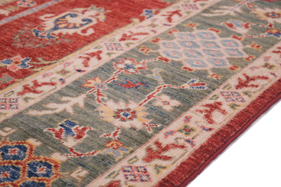 A close-up of a traditional patterned Afghan fine Aryana hand-knotted carpet showing a red edge, a sage green main border, and cream sections with blue and red floral motifs.