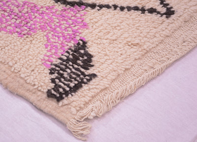 Vintage Azilal rug corner with light pink pile, black motifs, magenta accents, and fringe.