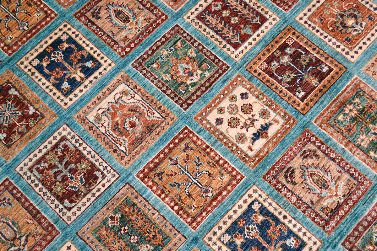 A close-up of a garden design Bakhtiari design turquoise carpet area rug featuring a grid of square panels in rust red, teal, cream, and navy blue with intricate floral and geometric motifs.