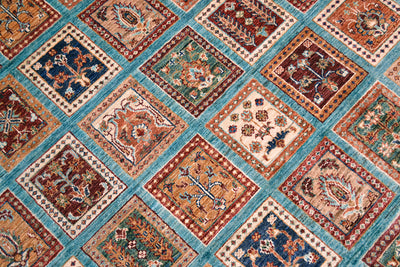 A close-up of a garden design Bakhtiari design turquoise carpet area rug featuring a grid of square panels in rust red, teal, cream, and navy blue with intricate floral and geometric motifs.