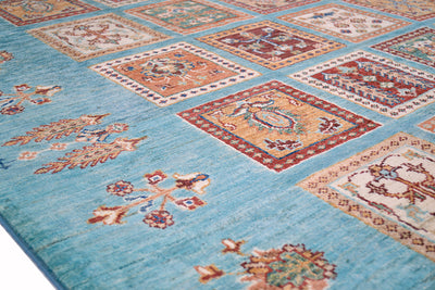 A close-up of a patterned handmade Afghan Bakhtiari area rug with a light turquoise-blue base and multiple rectangular medallion panels in rust red, beige, and cream.