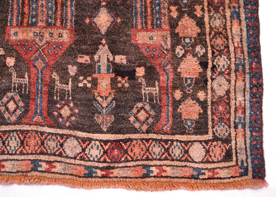 A close-up of an old patterned Belouch runner rug showing a dark brown field with red, beige, and blue geometric motifs and fringe along the bottom edge.