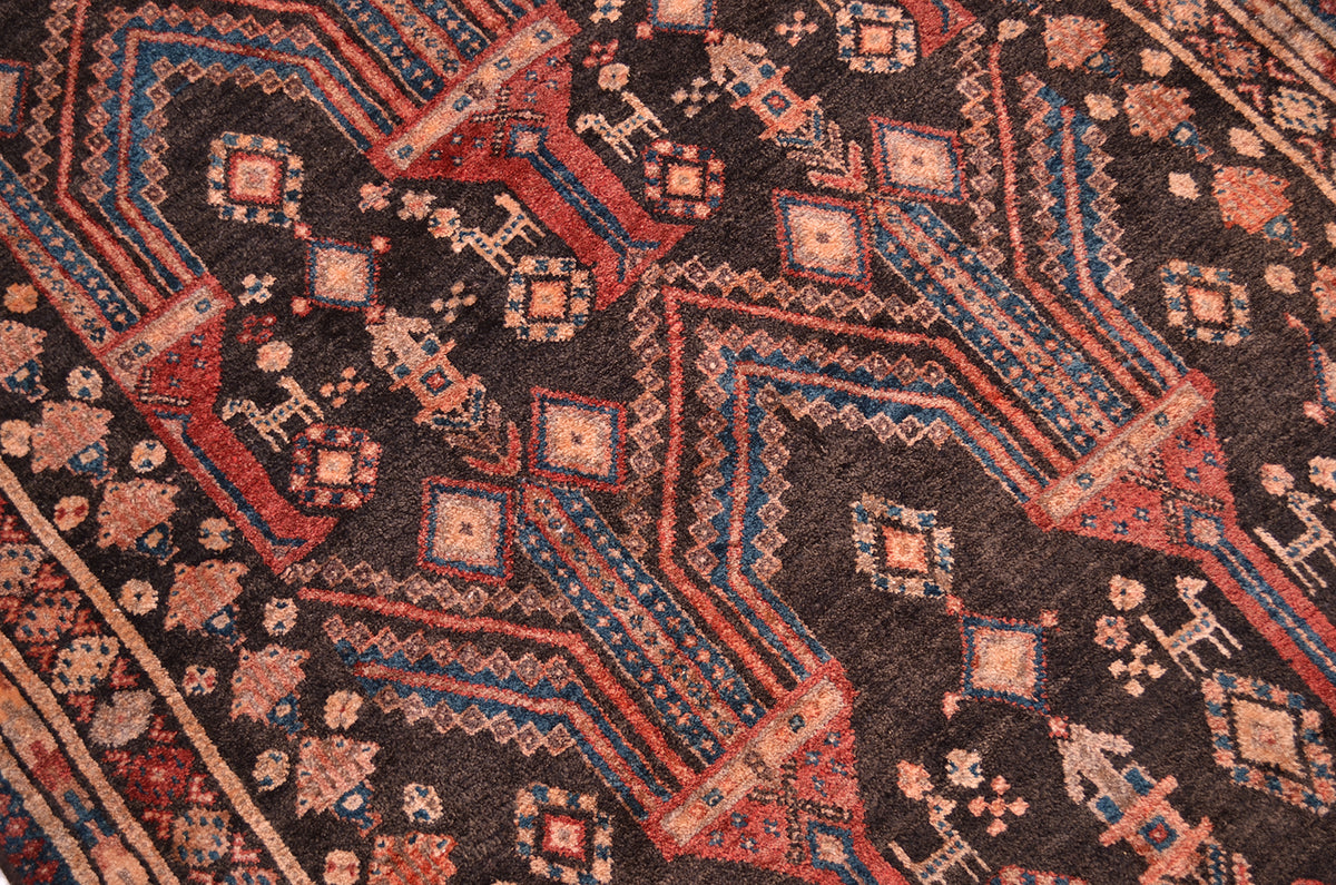 A close-up of a traditional patterned Old Belouch wide runner rug with a dark brown /charcoal base and geometric motifs in red, teal, and beige.