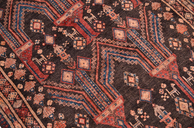 A close-up of a traditional patterned Old Belouch wide runner rug with a dark brown /charcoal base and geometric motifs in red, teal, and beige.