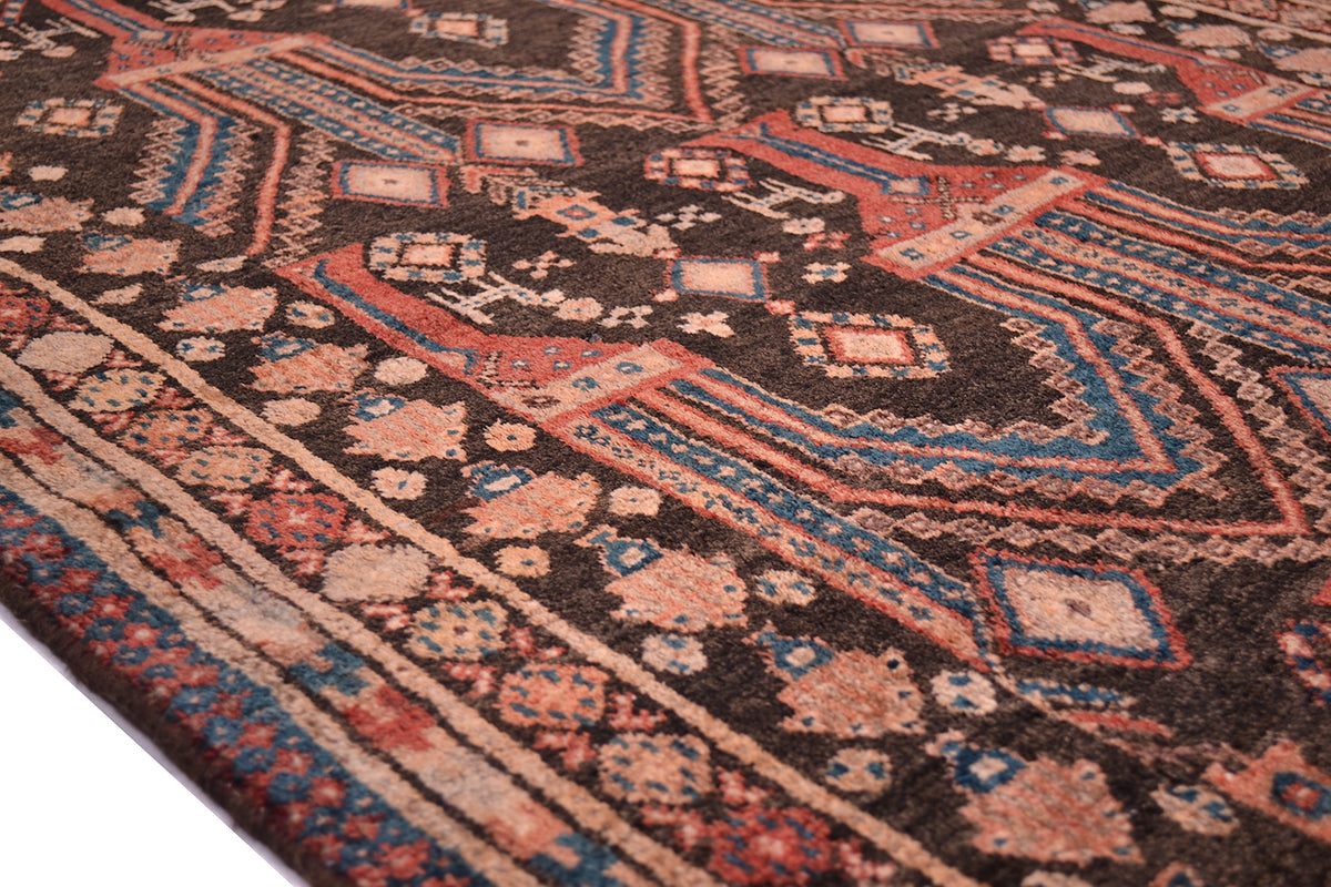 A close-up of a traditional Afghan patterned Belouch runner rug with a dark brown-charcoal base and geometric motifs in red, teal, beige, and cream.