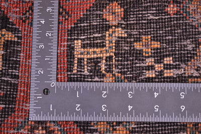 Close-up of the hand-knotted weave of an Old Belouch wide runner rug with a dark charcoal base and orange, rust, and red woven motifs, shown with metal ruler to show scale of the knot density.