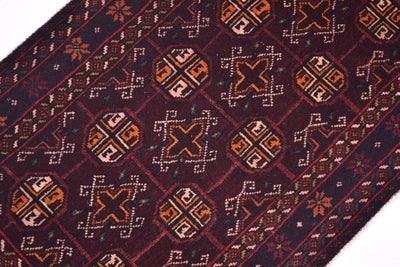 A close-up of a patterned Bokhara design Belouch mat with a dark burgundy background and geometric motifs in orange, beige, and white.