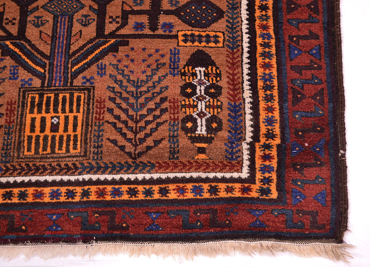A close-up of a traditional patterned belouch Afghan rug showing its detailed border and fringe. The rug features a warm brown field with geometric and tribal motifs in orange, blue, black, and cream, set against a plain white background.