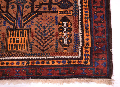 A close-up of a traditional patterned belouch Afghan rug showing its detailed border and fringe. The rug features a warm brown field with geometric and tribal motifs in orange, blue, black, and cream, set against a plain white background.