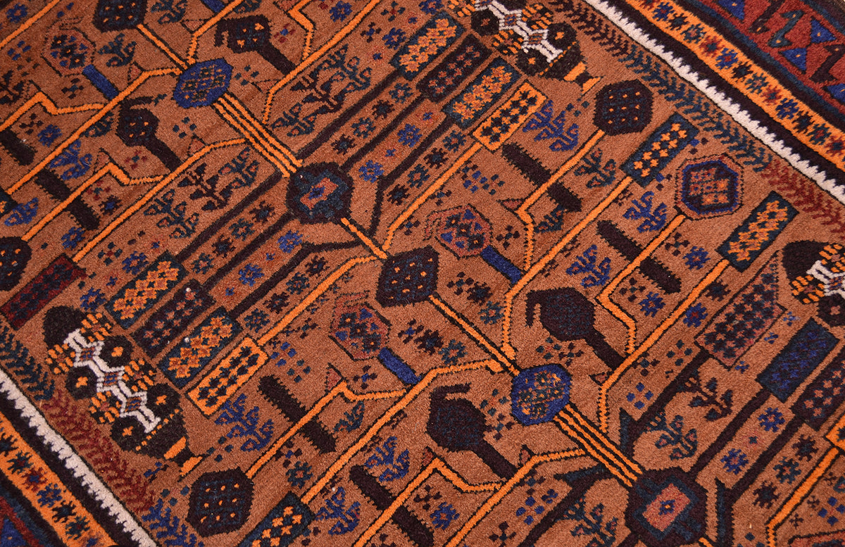A close-up of a patterned Belouch Afghan rug with a warm cinnamon brown base, featuring geometric and tribal-inspired motifs in dark brown, black, orange, and blue.