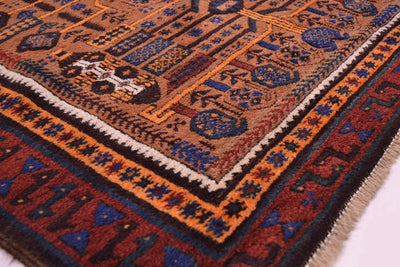 A close-up of a traditional patterned Afghan belouch tribal rug showing its detailed woven design, featuring geometric motifs in orange, brown, blue, red, and cream with a fringed edge.