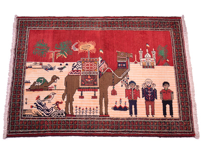 A rectangular handwoven Pictorial Belouch rug with a red and beige central scene featuring an camel, birds, and human figures, surrounded by a dark patterned border and pink fringe on a white background.