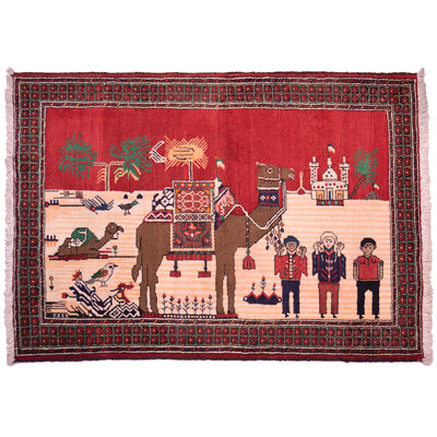 Hand-knotted wool pile Afghan Pictorial Belouch rug depicting camels and people in the foreground with a mosque in the background and a red sky.