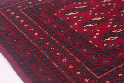 A close-up of a traditional patterned small Belouch rug with a deep red field, dark brown borders, and cream geometric motifs.