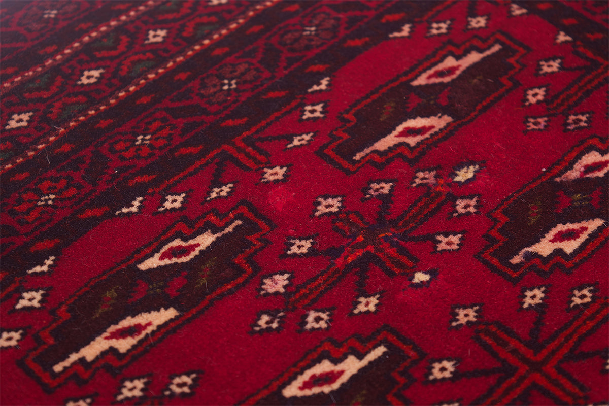 A close-up of a red patterned Belouch mat with geometric motifs in dark brown, black, and cream.