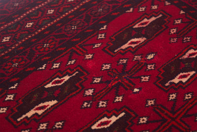 A close-up of a red patterned Belouch mat with geometric motifs in dark brown, black, and cream.
