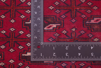 A close-up of the hand-knotted back of a red Belouch mat with geometric motifs, shown with a black metal ruler to show scale of the knot density.