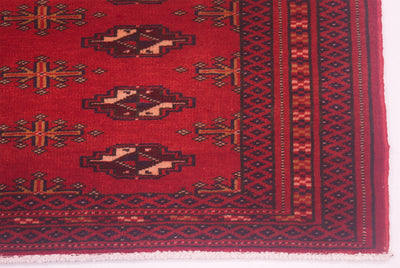 A close-up of a handmade red Afghan Belouch mat showing geometric motifs and a dark border.