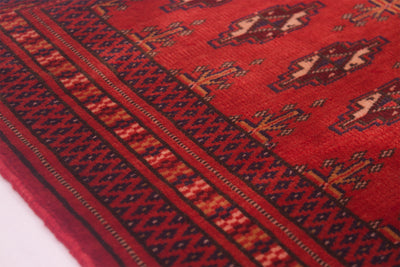 A close-up of a red patterned small Belouch rug with dark navy and beige geometric borders and motifs.