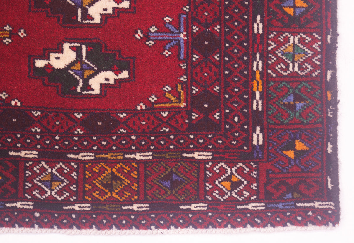 A close-up of a traditional patterned Afghan Belouch mat showing a deep red field with geometric borders and motifs in dark blue, cream, yellow, and orange.