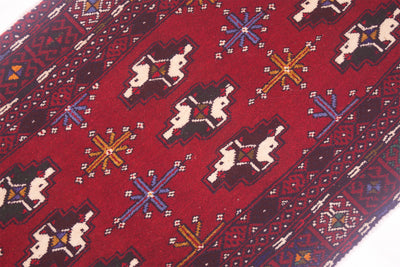 A close-up of a traditional patterned Afghan Belouch mat or small rug with a deep red field, featuring geometric star motifs in blue, yellow, and white, and stylised emblems.