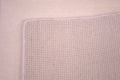 Close-up of the hand-knotted back of a woven rug corner showing a textured plain off-white Indian runner with a matching bound edge.
