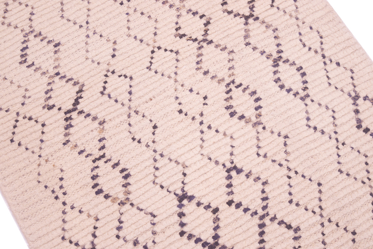 A close-up of a woven runner or rug in a cream color with a dark charcoal gray geometric diamond pattern.