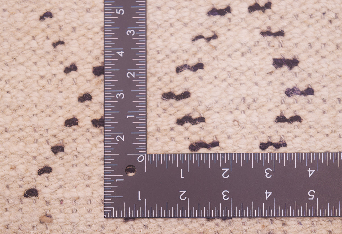 Close-up of a cream rug with charcoal design, shown with a metal L-square ruler for scale.