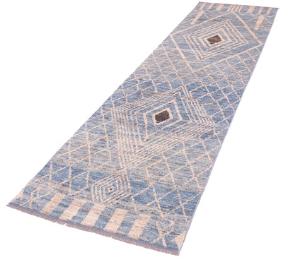 A long rectangular area runner with a geometric diamond pattern in light blue and beige, featuring a small dark brown accent in the center and fringed edges, shown on a plain white background.