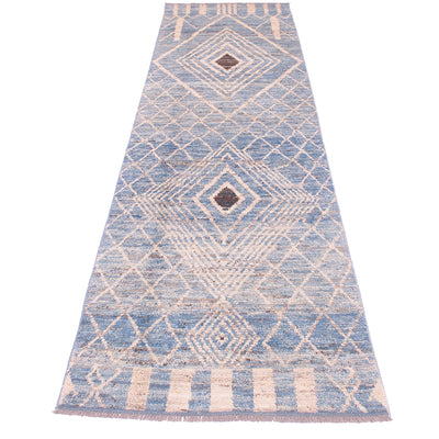 A long rectangular area runner/rug with a blue and beige geometric diamond pattern and fringe on the ends, shown flat against a white background.