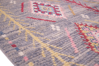 A close-up of a textured Berber style area rug with a light blue-grey base and multicoloured geometric patterns in red, yellow, pink, and white.