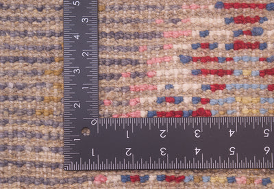 Close-up of the hand-knotted weave of a textured Afghan Berber design rug with a dark ruler placed along the edge to show scale of the weave, featuring a multicolour pattern of beige, blue, pink, and red.