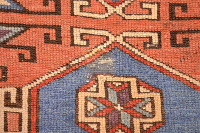 Antique rug close-up with orange and blue medallion and geometric motifs