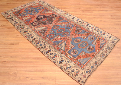 Antique Bergama rug laid diagonal on wood floor, featuring rust, blue, and beige motifs