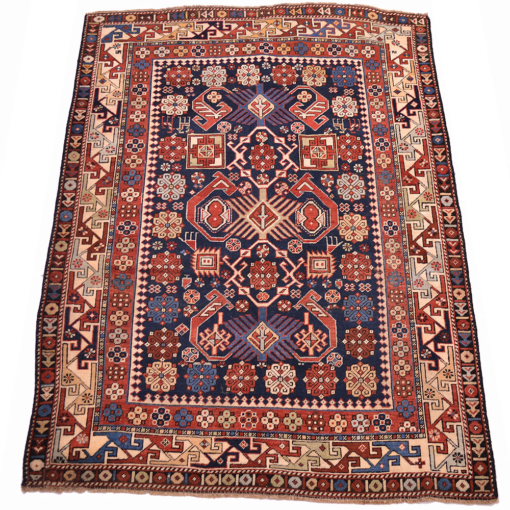 Antique rug with navy center, red-orange floral motifs, cream corner details, patterned border.