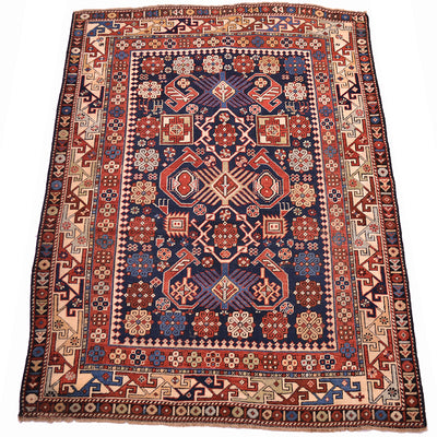 Antique rug with navy center, red-orange floral motifs, cream corner details, patterned border.