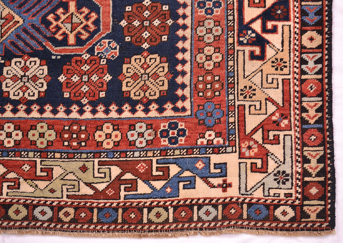 Rug corner close-up with navy border, red accents, and repeating cream geometric trim.