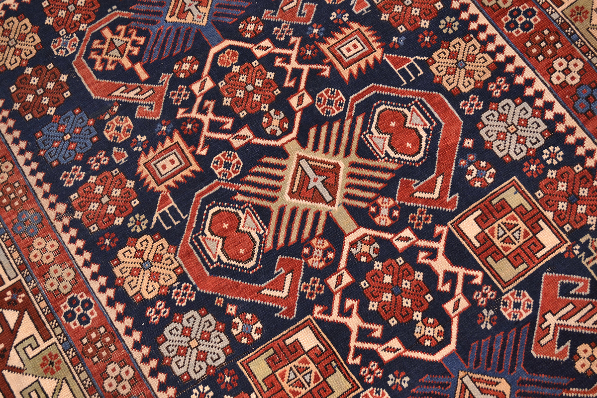 Rug close-up showing navy ground with red-orange rosettes and cream geometric details.