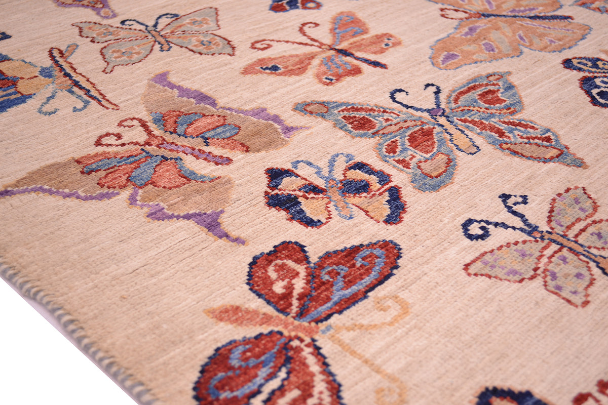 Close-up of a hand-knotted Afghan Butterflies rug with a beige background and a repeating butterfly pattern in muted red, blue, purple, and tan tones.