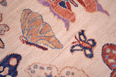 Close-up of an Afghan patterned butterflies rug with butterfly motifs in peach, blue, rust, and purple on a warm beige background.