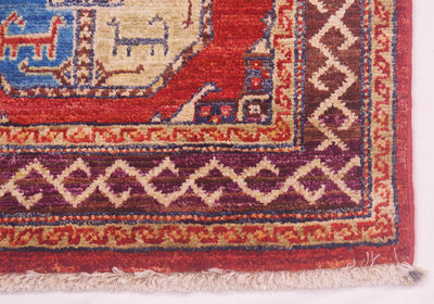 Close-up of a patterned Ersari design small rug corner showing a red field, cream and burgundy geometric border, and fringed edge.