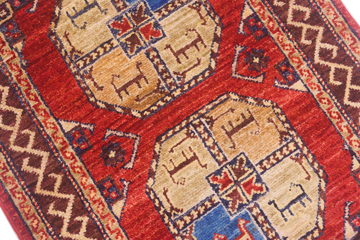 A close-up of a traditional patterned Afghan Fil Pai Mat featuring a deep red field with two large beige medallions, accented by blue and brown geometric motifs and borders.