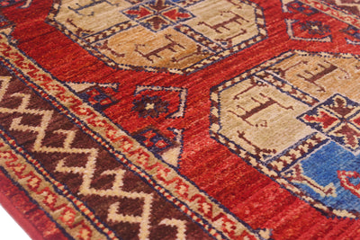 A close-up of a traditional patterned Fil Pai small rug with a deep red field, beige geometric motifs, and a dark brown border with cream and blue details.