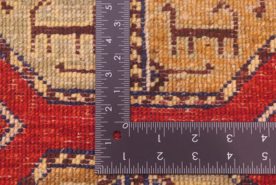 Close-up of the hand-knotted weave of a patterned Afghan Fil Pai small rug with a dark metal L-shaped ruler placed over it for scale of the knotting, showing a red, beige, and brown woven design.