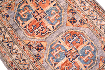 A close-up of a traditional patterned Afghan elephants foot design small rug featuring geometric medallions in rust orange, dusty blue, beige, and grey.