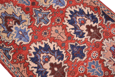 A close-up of a traditional patterned Afghan Chobi small rug with a red field, featuring large blue and beige floral motifs and a blue border.